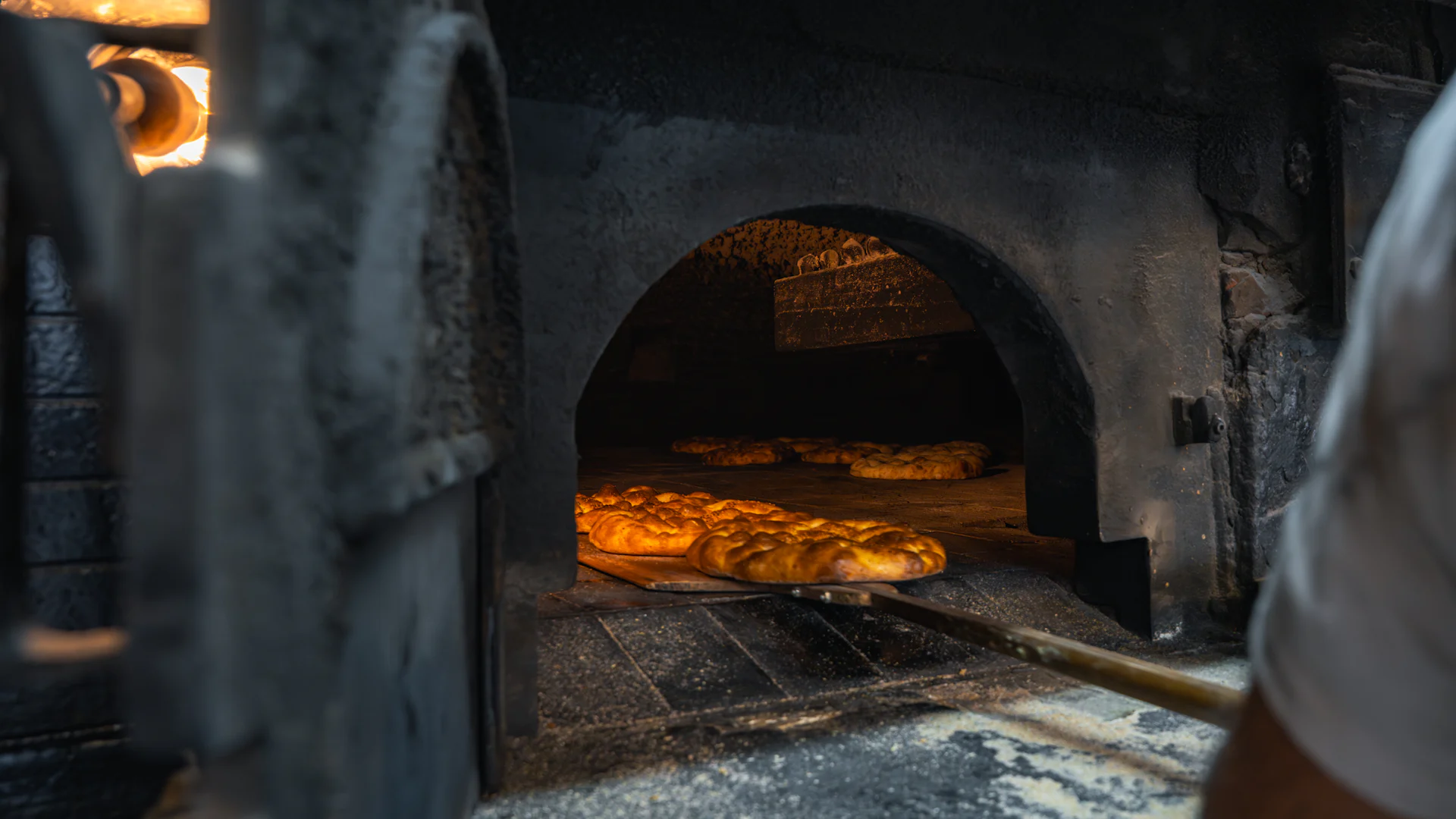 A baker's peel reaching into a wood-fired stone oven, loaves lit by the embers inside
